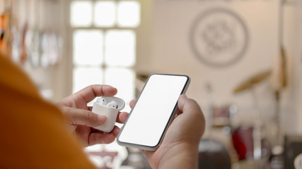 Cropped shot of male holding wireless headphone and blank screen smartphone