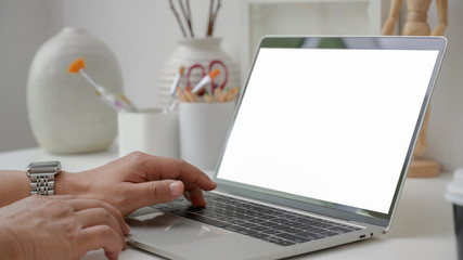 Cropped shot of designer typing on blank screen laptop in minimal workspace with panting tools and decorations