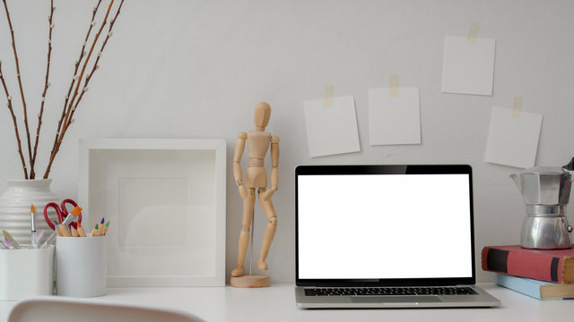 Close up view of designer workplace with blank screen laptop, books, painting tools and decorations on white table