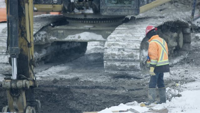 Construction working directing excavator on winter construction site on snowy day - side profile