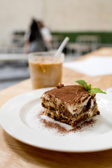 Close up a plate of Tiramisu cake with a glass of ice coffee latte in a modern cafe background