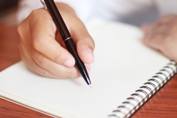 A woman's hand writing a book on a wooden desk.