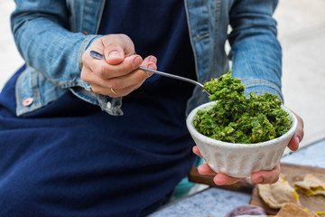 Green pesto dip paste with walnuts, seeds, nuts, parsley, basil, dill, mint, cilantro herbs and oil. Woman holds pesto