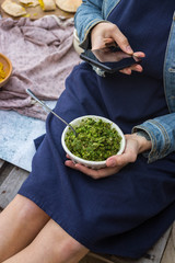 Woman hands take picture of food at home or cafe with smartphone. Phone photo of green basil walnuts pesto paste for blogging or social media. Vegan and vegetarian healthy diet.