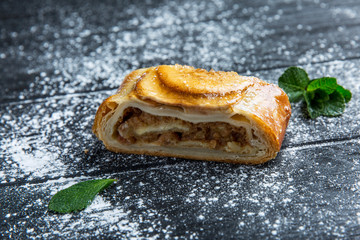 Traditional apple strudel with icing sugar on a dark wood table. Close-up.