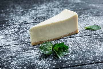 Cheesecake with icing sugar on the table of their dark wood. Close-up.