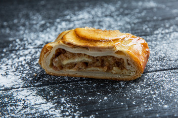 Traditional apple strudel with icing sugar on a dark wood table. Close-up.