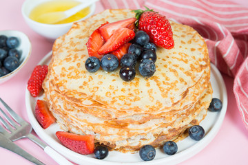 Thin traditional Russian pancakes on a trendy pink background with berries and honey. Close up