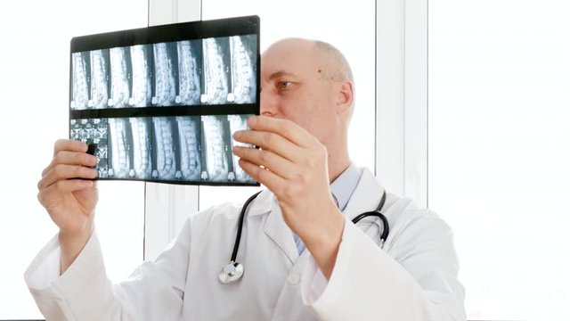 Doctor looking at X-ray of backbones and nodding head YES. Serious middle aged male doctor in white coat with stethoscope examining X-ray image in hospital