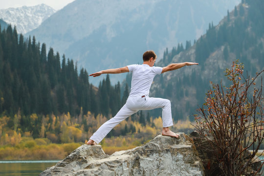 A man practices yoga on a background of mountains. Pose Virabhadrasana 2 or warrior