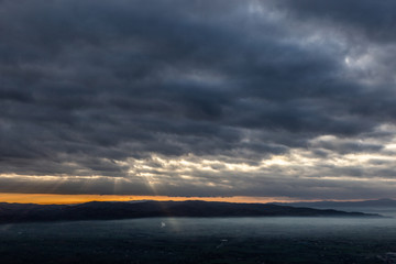 Sun rays coming down from some clouds over a valley filled by fog, illuminating part of it