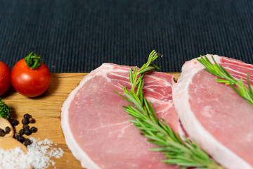 Raw pork chop meat on wood plate with vegetables, spices, salt and black pepper in dark black cloth table