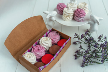 Gift set of sweets from macarons and marshmallows beautifully photographed in a box on a white wooden table with flowers