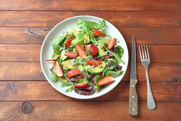 Avocado salad with strawberries, blue cheese, arugula and beet leaves on wooden background. Healthy lunch bowl Vegan healthy food concept