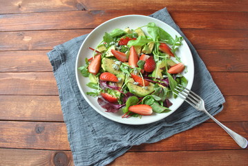 Avocado salad with strawberries, blue cheese, arugula and beet leaves on wooden background. Healthy lunch bowl Vegan healthy food concept