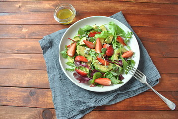 Avocado salad with strawberries, blue cheese, arugula and beet leaves on wooden background. Healthy lunch bowl Vegan healthy food concept