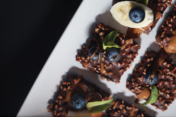 Chocolate dessert with nuts and fresh berries. Sweet snack for coffee biscuit in glaze and nut crumbs with fruit.