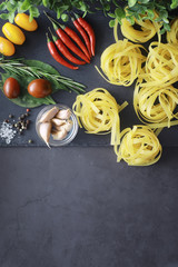 Pasta on the table with spices and vegetables. Noodles with vegetables for cooking on a black stone background.