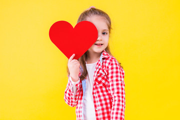 Pretty fair haired girl in pink checkered shirt is hiding behind red paper decorative heart sign....