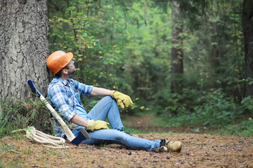 Naklejka na ściany i meble Male lumberjack in the forest. A professional woodcutter inspects trees for felling.