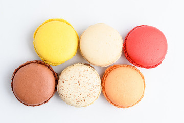 Top view of six sweet French macarons with different aromas, isolated on white, flavours of lemon, caramel, vanilla, orange and chocolate, tasty dessert in pastel colors on a table