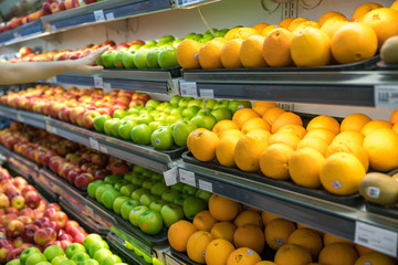 Fresh healthy fruits on shelves in supermarket. With a woman hand choosing best fruits