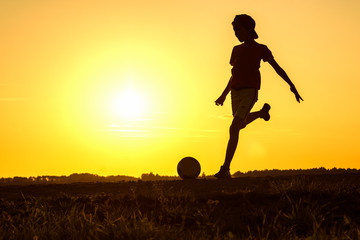 Boy playing football, teen exercising in nature at sunset, silhouette of playing child at sunset in countryside