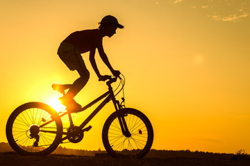 Fototapeta na wymiar Boy , kid 10 years old riding bike in countryside, teenager making trick on bycicle, silhouette of riding person at sunset in nature