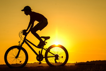 Boy , kid 10 years old riding bike in countryside, teenager making trick on bycicle, silhouette of riding person at sunset in nature
