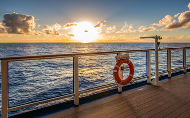 Sunset on cruise vacation. Sun just above the horizon and promenade deck with railing in the front. - obrazy, fototapety, plakaty