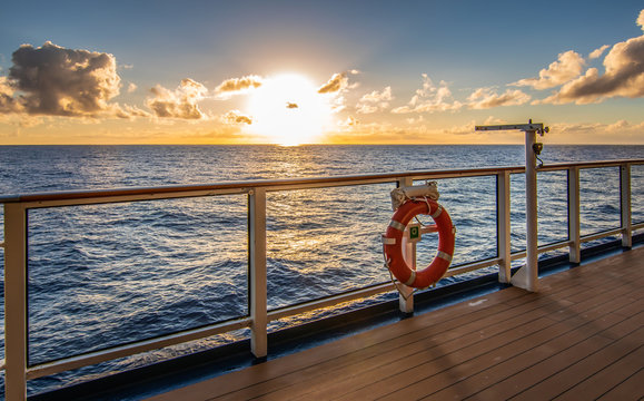 Sunset on cruise vacation. Sun just above the horizon and promenade deck with railing in the front.