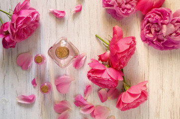 Rose water and oil in glass bottle and fresh flowers on branch on wooden background, SPA and aromatherapy concept