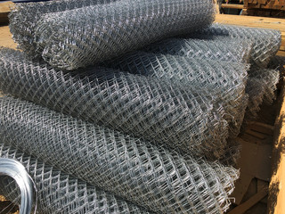 Fototapeta na wymiar Metal mesh netting rolled into rolls and coils of steel wire. Rolled chain-link fence