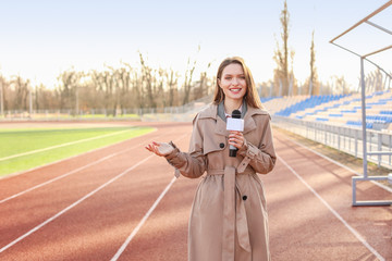Beautiful reporter with microphone at the stadium - obrazy, fototapety, plakaty