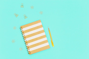 Workspace concept for school or office. Flat lay with closed notebook on spring, yellow colored pencil, golden paperclip from metal on paper background mint colors  with copy space. 