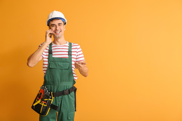 Handsome male worker talking by phone on color background