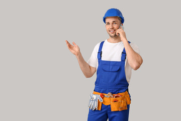 Handsome male worker talking by phone on grey background