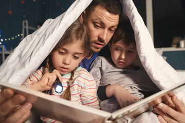 Father and his little children reading bedtime story at home