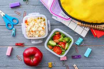 School lunch boxes with tasty food and stationery on wooden background