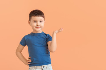 Cute little boy showing something on color background