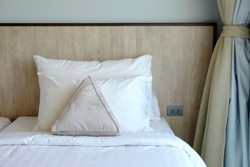 Front view of pillows and wooden headboard with white blanket beside the curtain