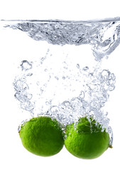 Falling of fresh limes into water against white background