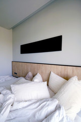 Empty black photo frame over unmade bed with white pillows, blanket and bedsheet