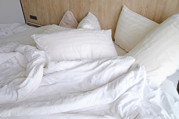Unmade bed with white pillows, blanket and bedsheet
