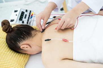 Asian middle age women undergoing acupuncture treatment with electrical stimulator on back or...