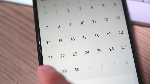 Close-up of a man's hand using a smartphone calendar application.