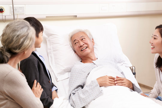 asian grandchild talking to grandpa in hospital ward