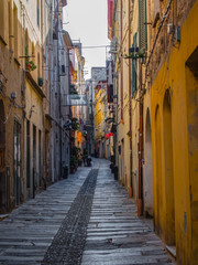 Fototapeta na wymiar Sassari via Turritana, colorful houses overlook the long stone road. Narrow alley amidst buildings in city