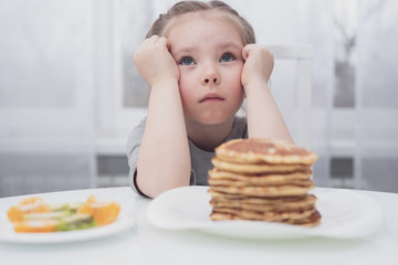 Diet for children. Sad and unhappy little girl. A child looks at a stack of pancakes.
