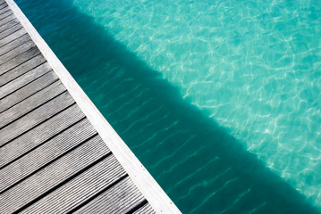 Abstract diagonal view of shallow tropical blue crystal waters sparkling under a weathered wooden...